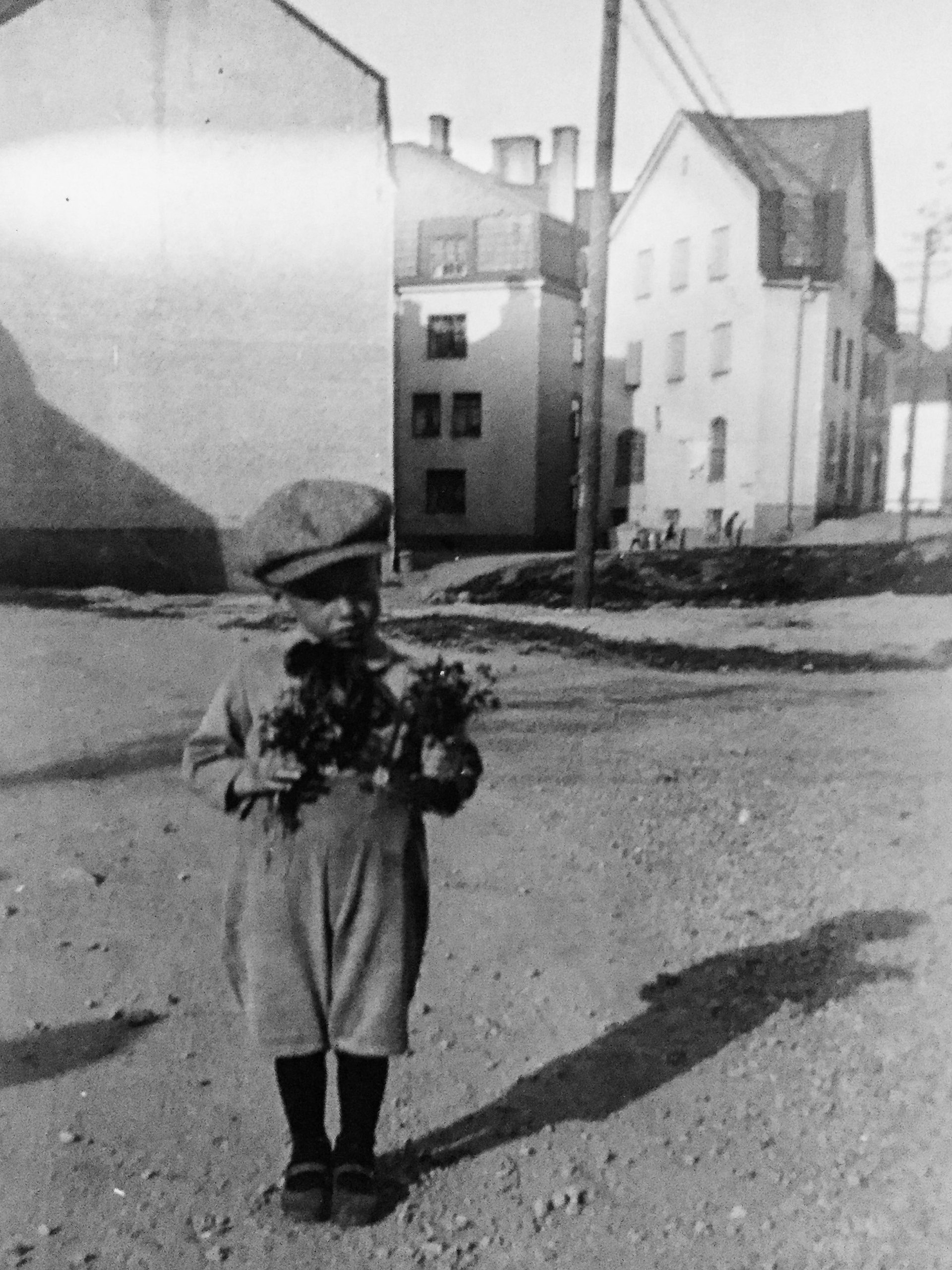 Svartvit bild av liten pojke med blommor i famnen.